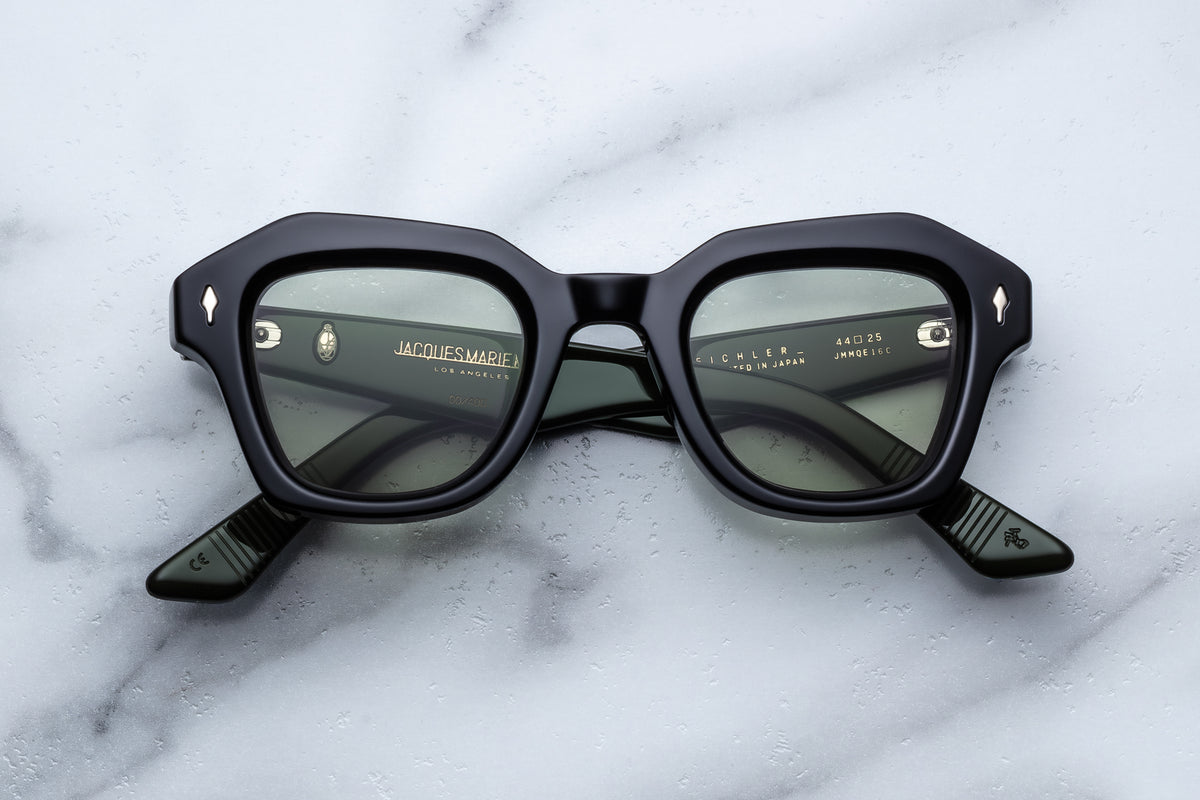 Black Jacques Marie Mage sunglasses with bold geometric frames and dark lenses resting on a pale marble surface